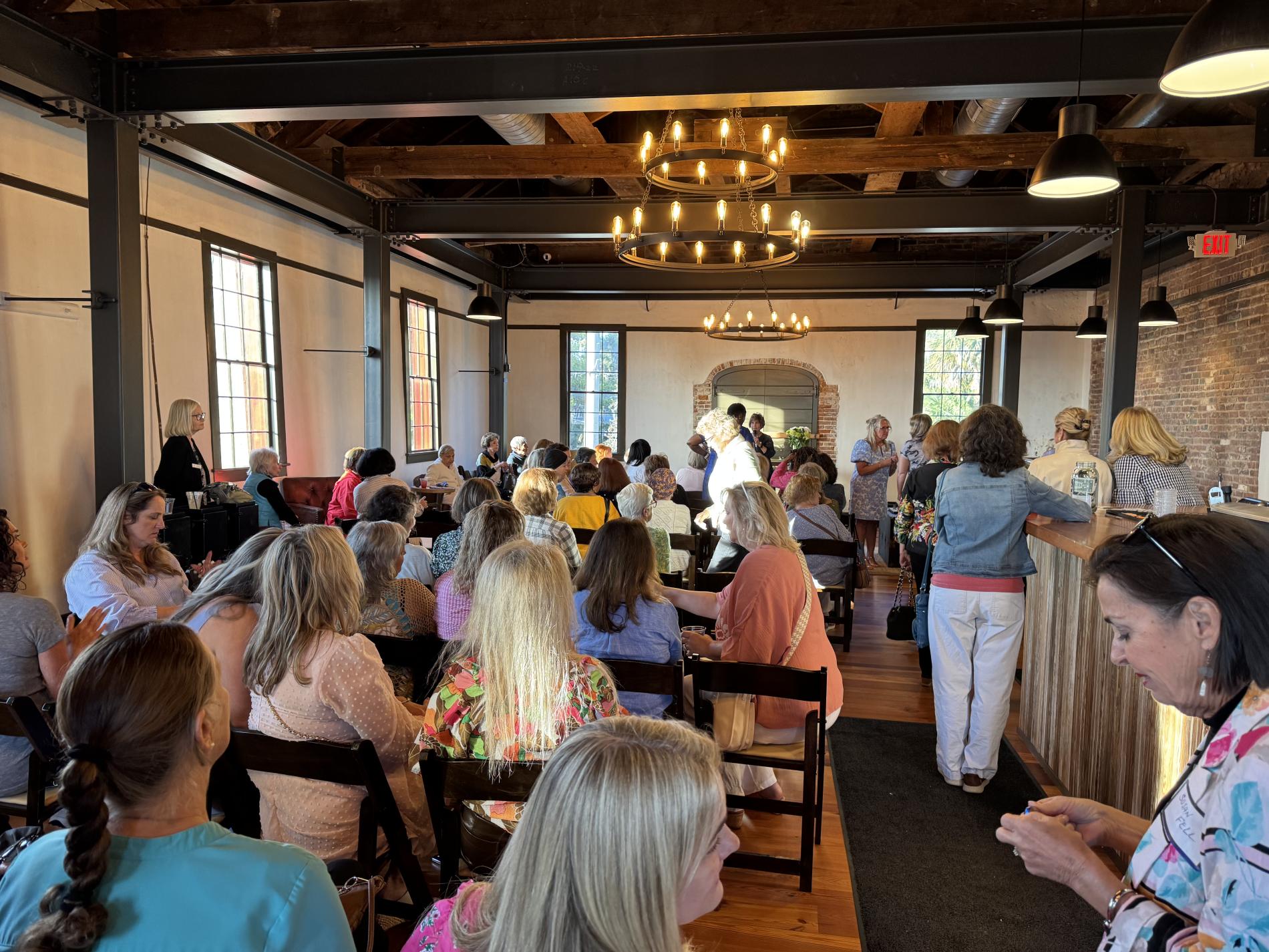 Guests seated indoors at a wedding ceremony with wooden beams and a chandelier overhead.