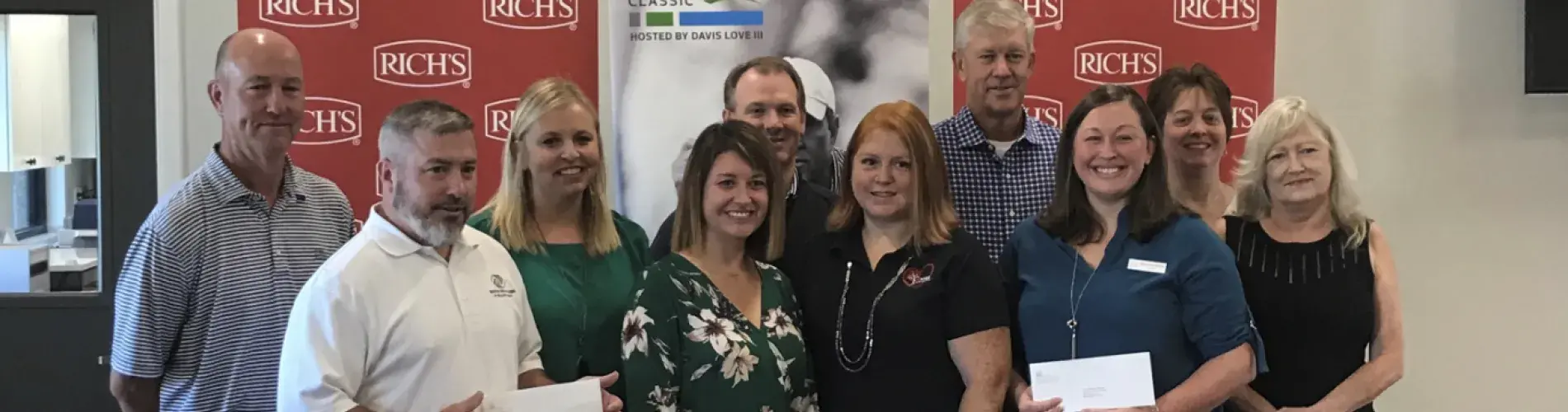 Group of people holding papers, smiling, standing indoors with banners in the background.