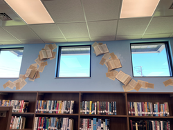 Books and pages decoratively displayed on a library wall beneath two windows.